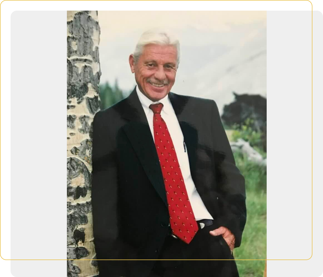 A man in suit and tie standing next to a tree.