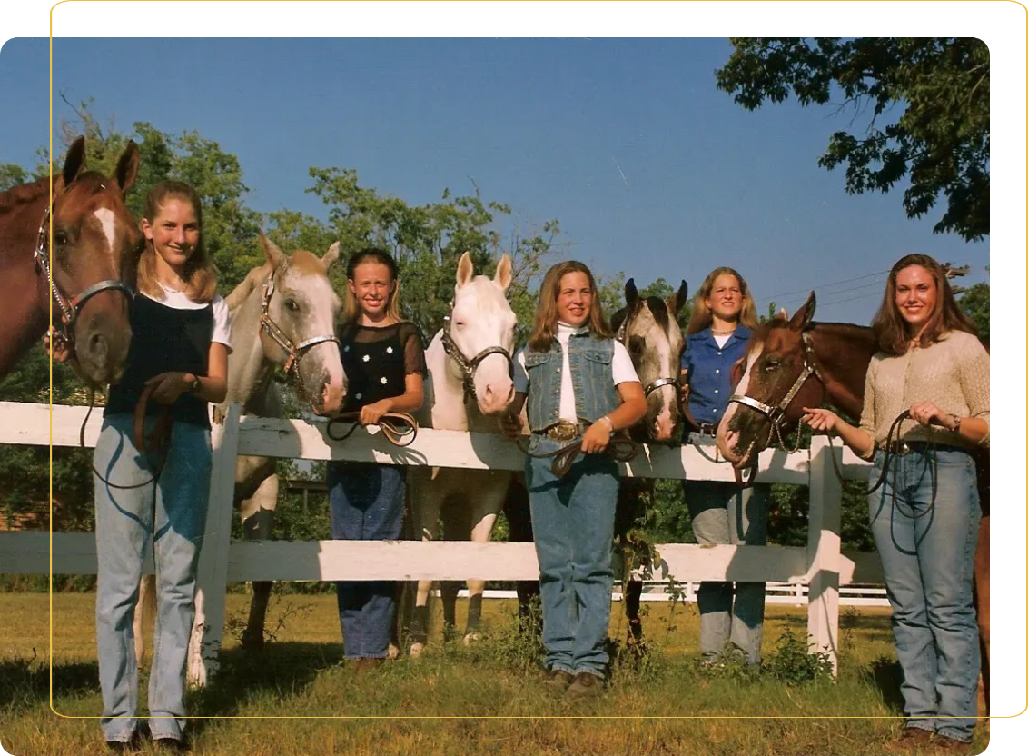 A group of people standing around horses on the grass.